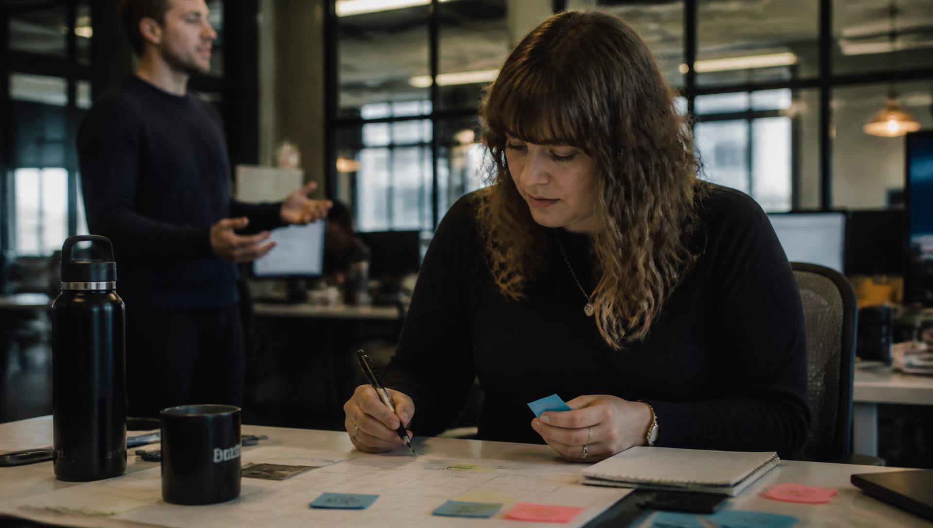 Marketing lead planning a campaign schedule at a workstation with a colleague behind